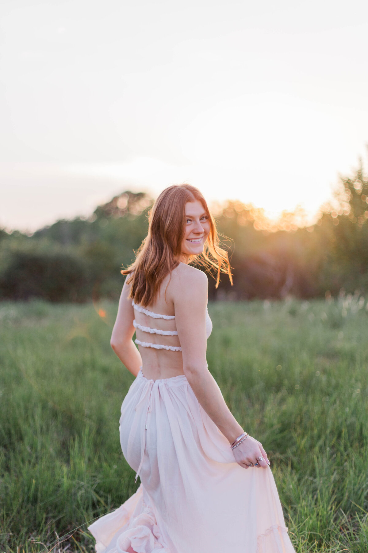 Highschool senior at sunset looks over her shoulder while the golden hour light makes her red hair glow