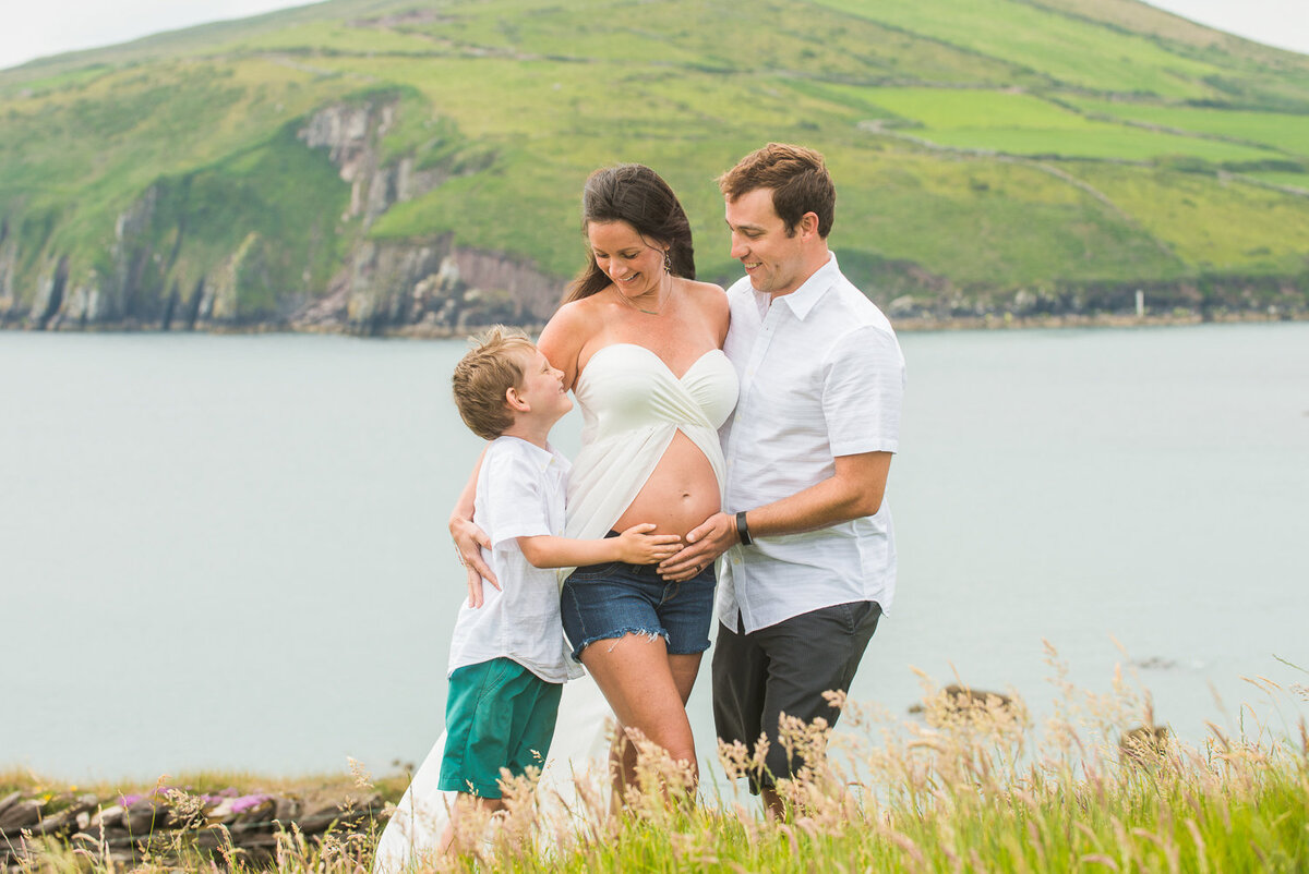 portrait of family of three with baby bump standing on a beach