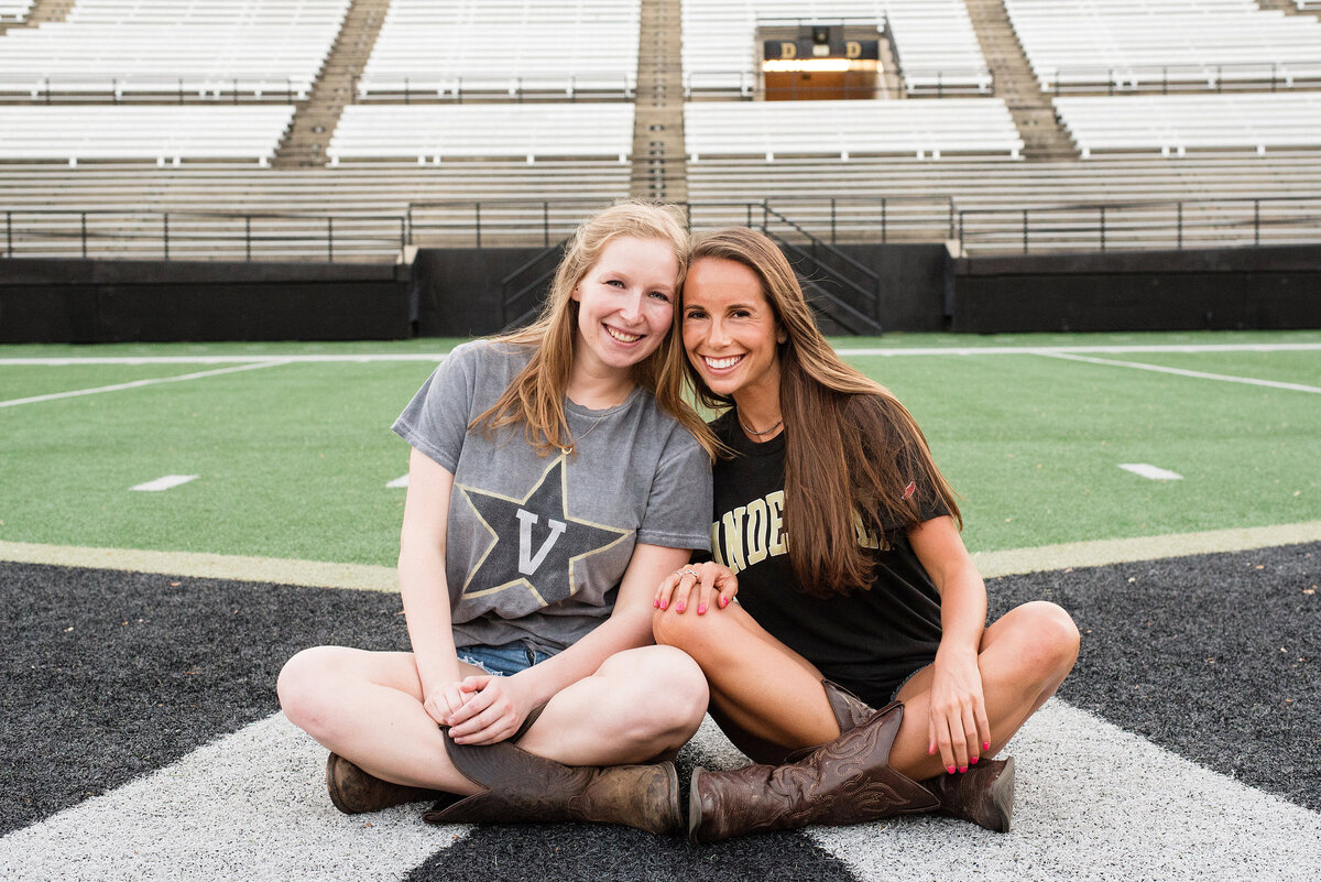 Two senior girls sitting on the football field wearing their Vanderbilt shirts