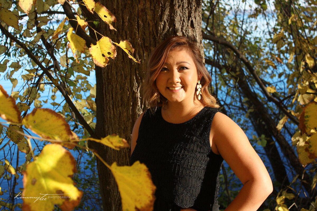 Pretty woman standing by a tree with yellow leaves by a lake