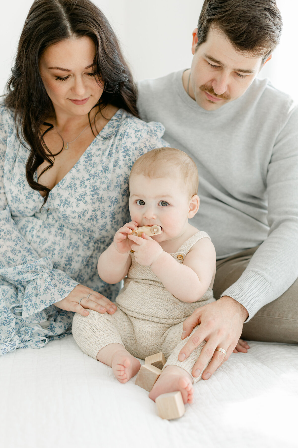 1 year old boy sitting with his mom and dad on a bed photographed by Family Photographer South Jersey Tara Federico