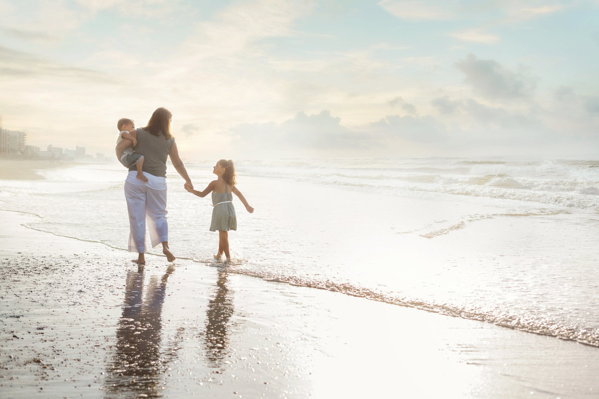 A mother and her two girls walk along the shore during a family photography session