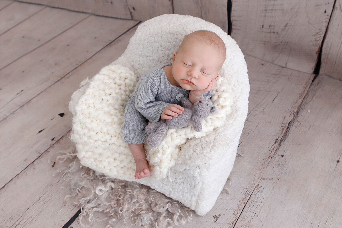 newborn-baby-sleeping-on-a-white-bed-holding-a-little-grey-teddy-bear