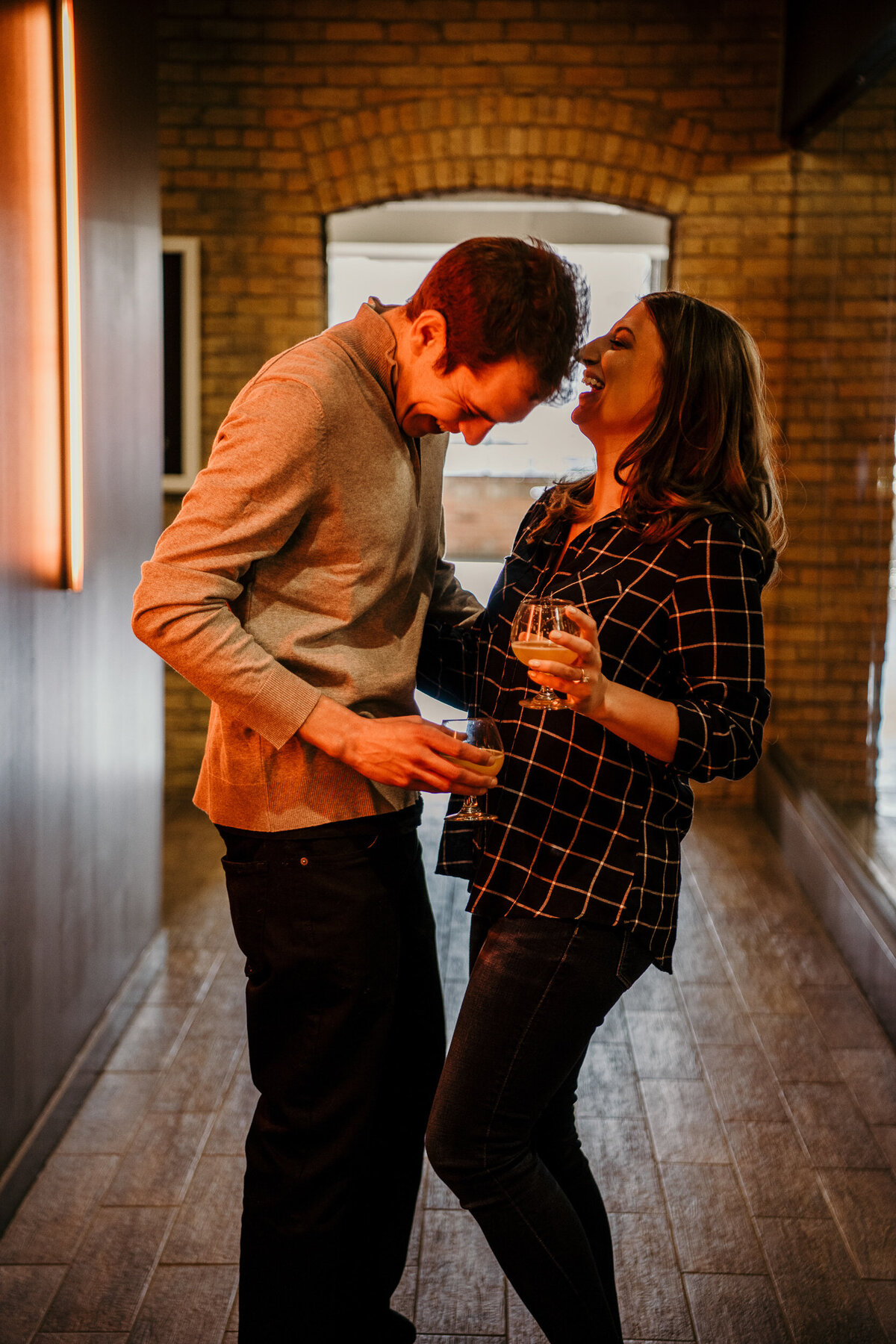 Woman and man laugh in a brewery hallway while holding drinks.