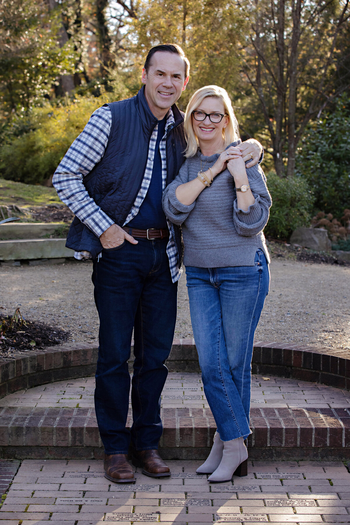 Elegant autumn portrait of parents standing together near brick terrace steps at UNCC Botanical Garden Charlotte NC, smiling confidently at the camera
