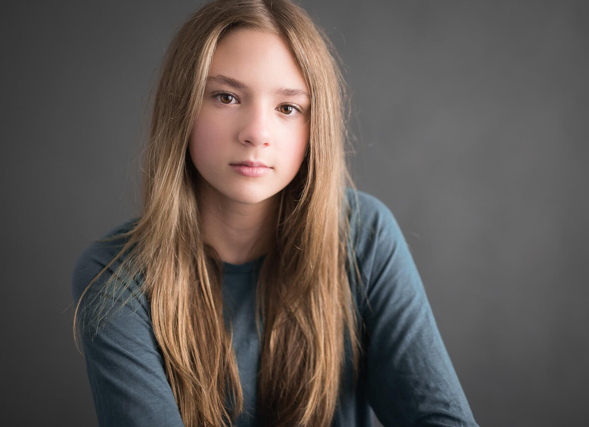 studio photo of a senior girl in a teal sirt with a serious expression and a grey background