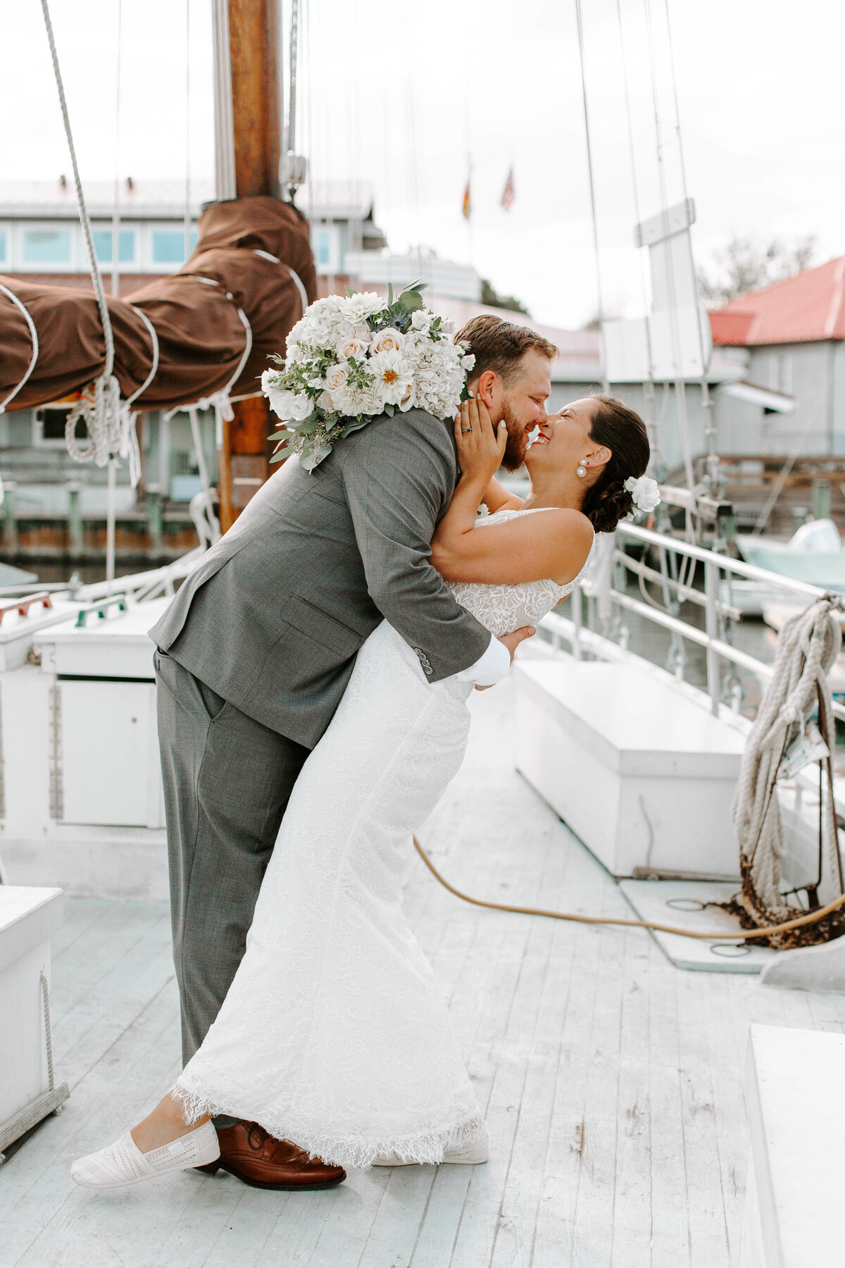 A bride and groom on a boat, about to kiss while the groom dips the bride back and they smile at eachother