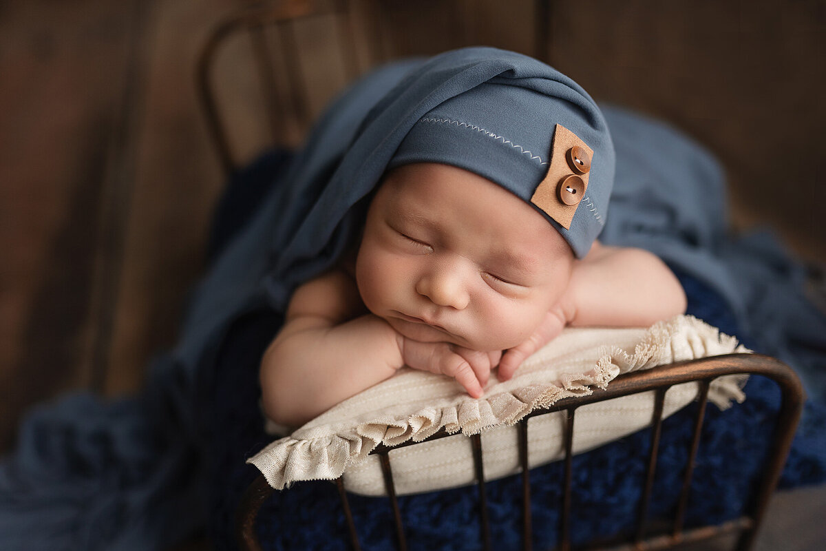 Baby boy wearing a blue bonnet, sleeping in an authentic water bucket during his newborn session.