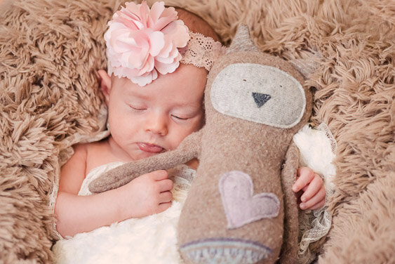 A newborn baby girl holding a brown stuffed toy at an Edmonton newborn photography session at home