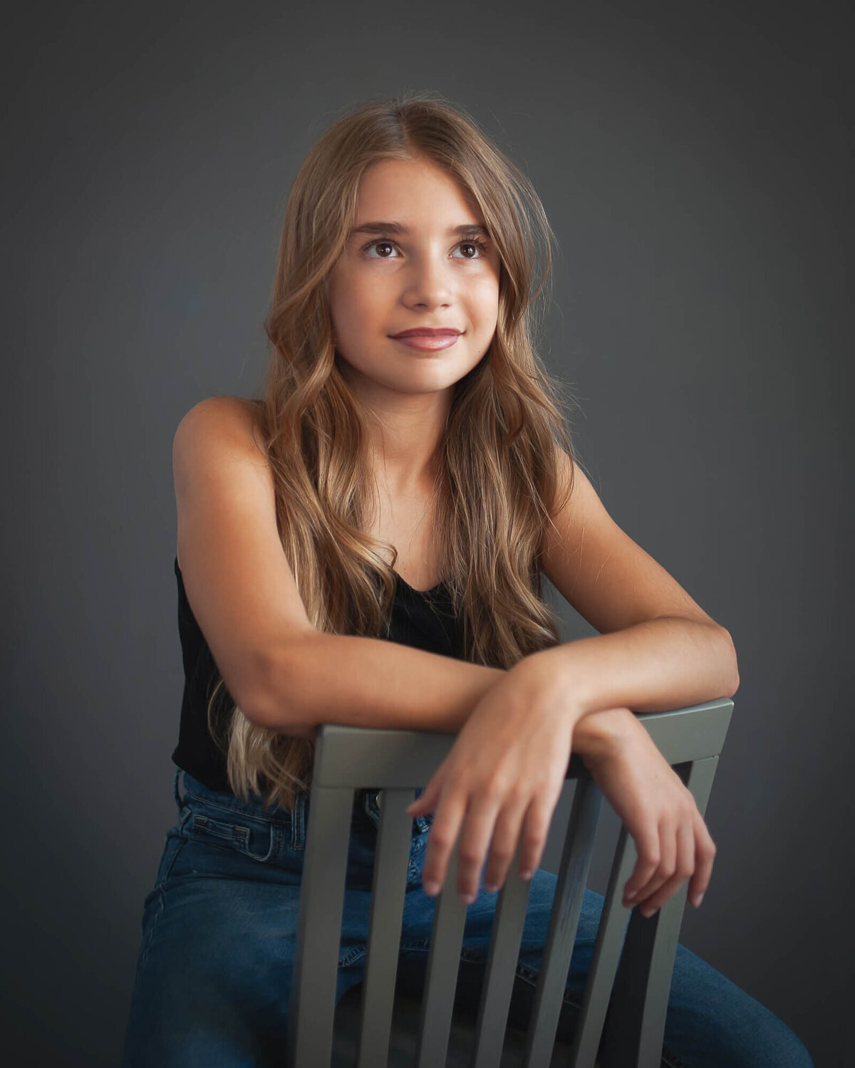 beautiful studio portrait of ten year old sitting backwards on a chair eyes looking up, grey background