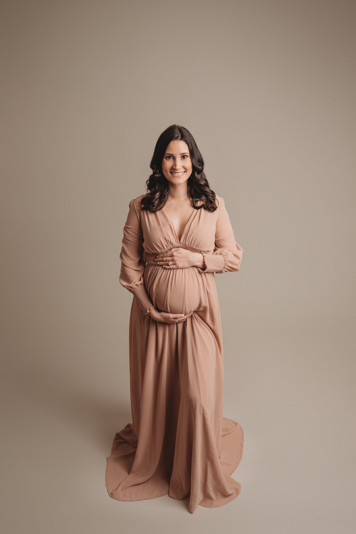 30 week pregnant woman wearing mauve long sleeve gown holding baby bump looking at camera