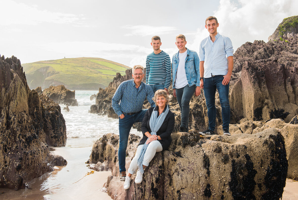 Family of five sitting on a large rock on a beach in Ireland, wearing denim