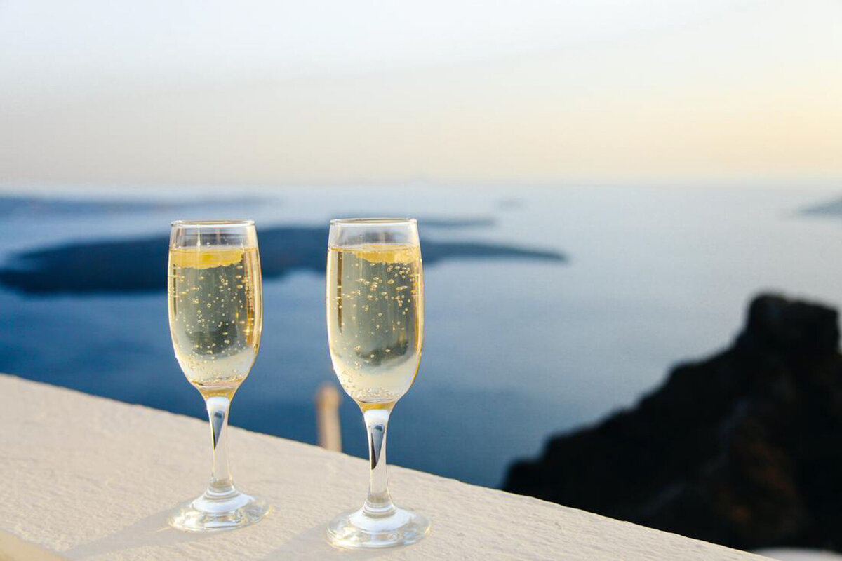 two glasses full of white wine with an ocean view behind