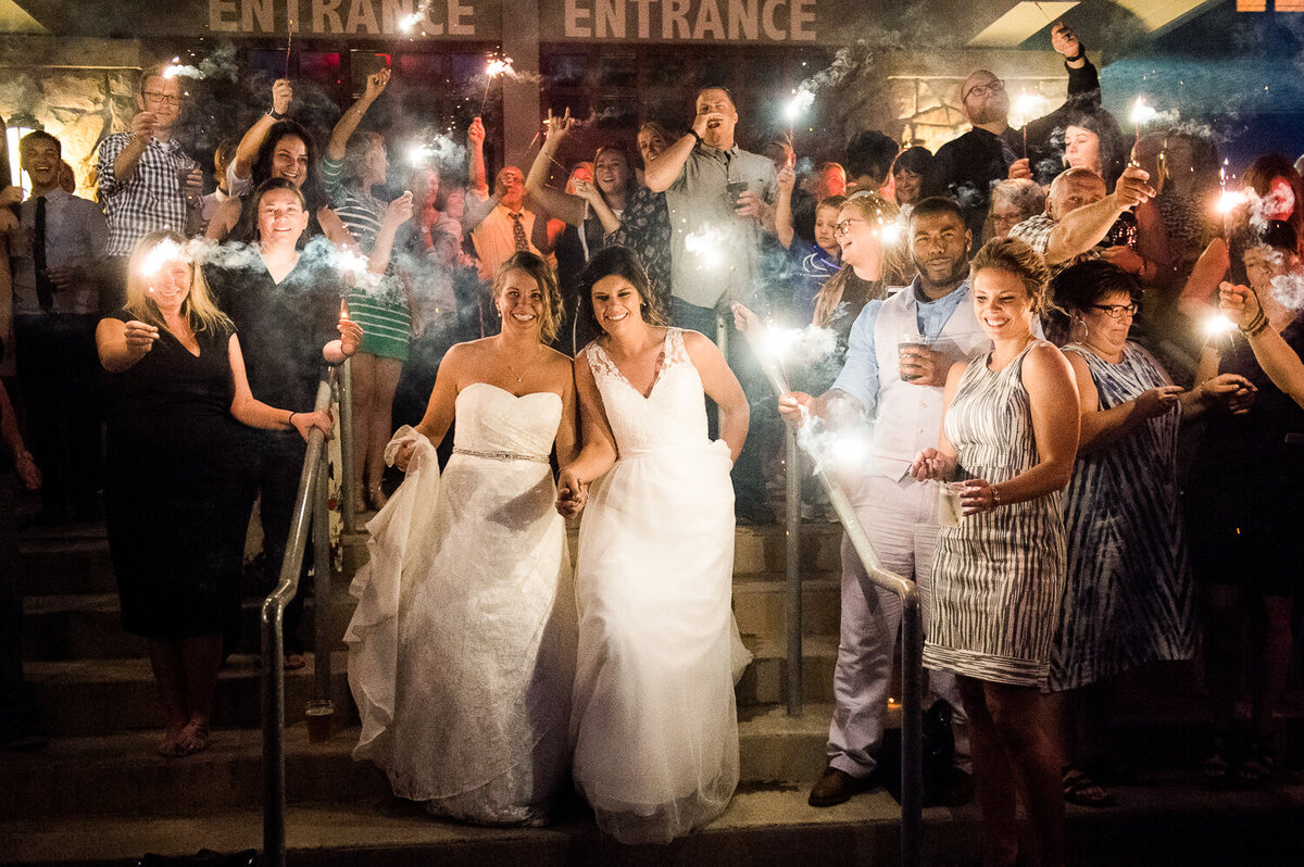 Lesbian couple stand with their guests holding sparklers at the end of the wedding day.