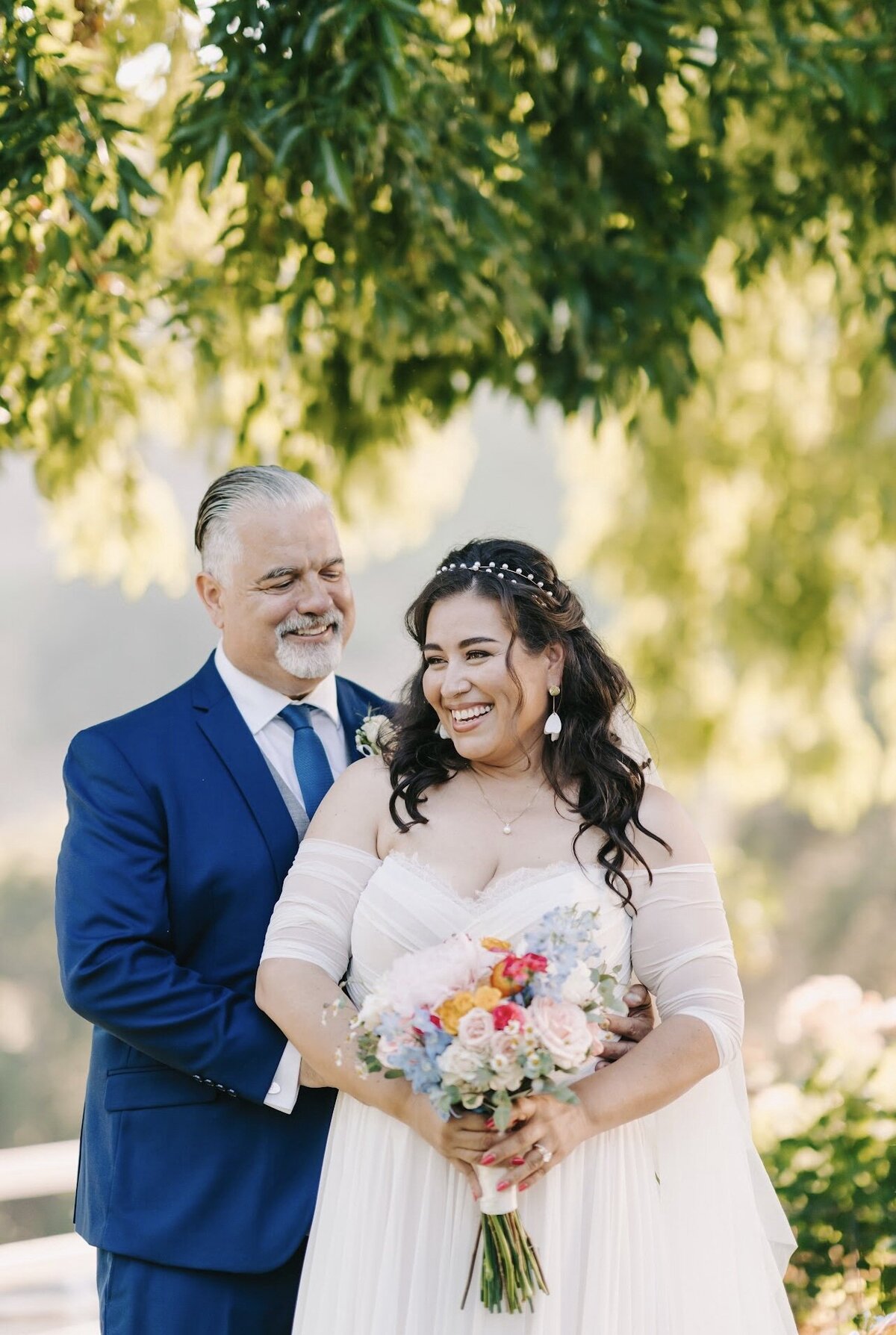 A bride stands in an outdoor setting with  her father
