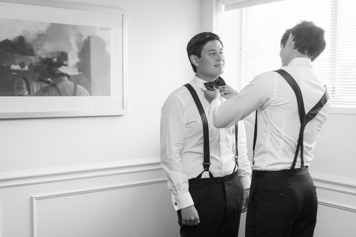 black and white wedding photo of groomsmen helping groom with bow tie at The Garden City Hotel