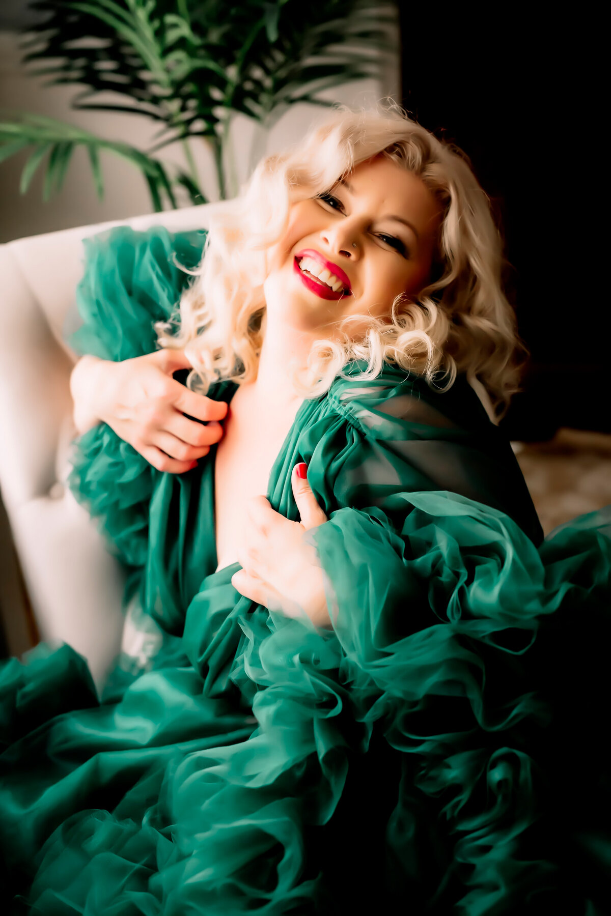 playful image of a woman posing in a green tulle robe laughing at the camera for her boudoir photoshoot