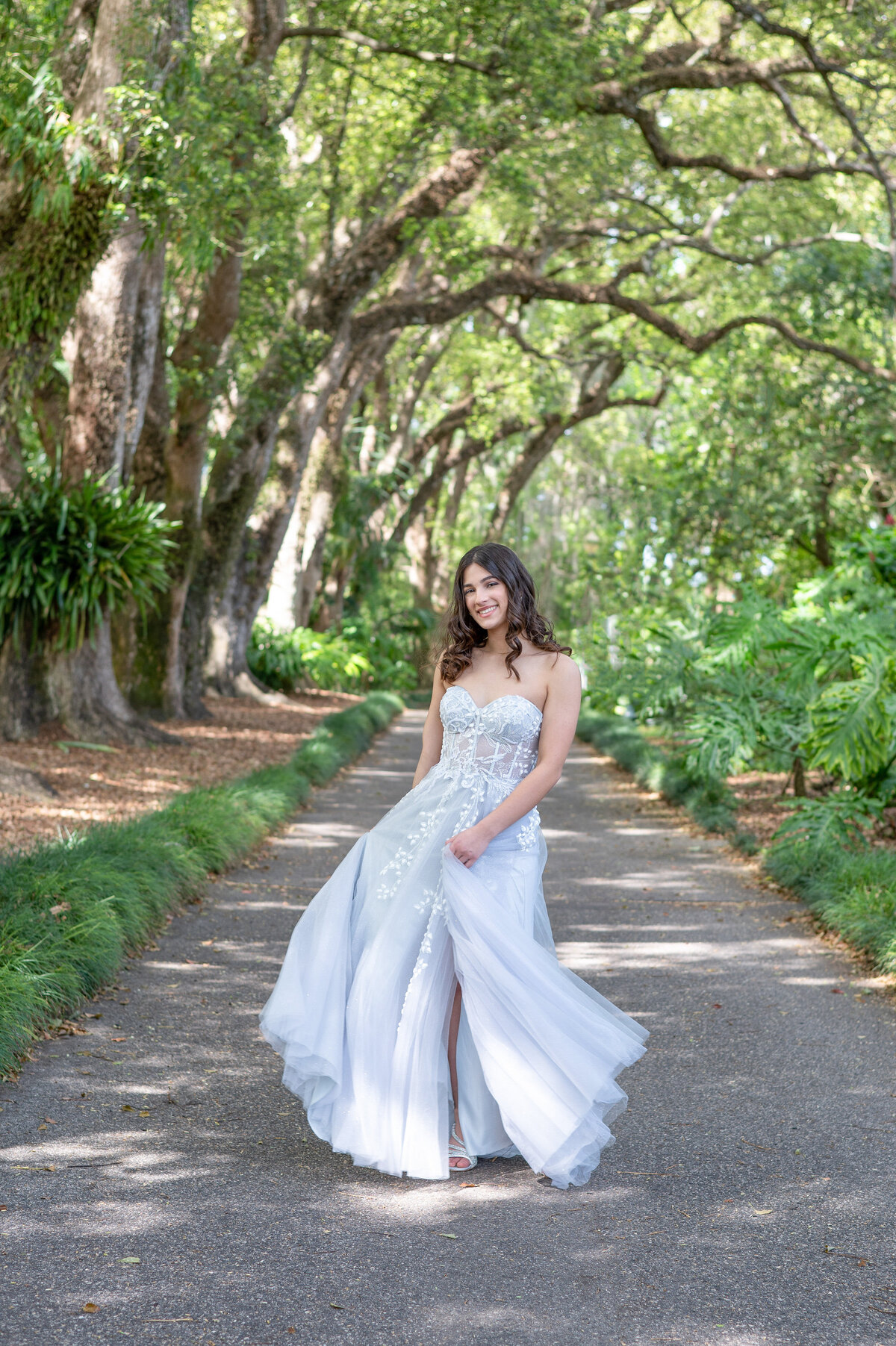 High school senior girl in floor length prom dress twirling in middle of path.