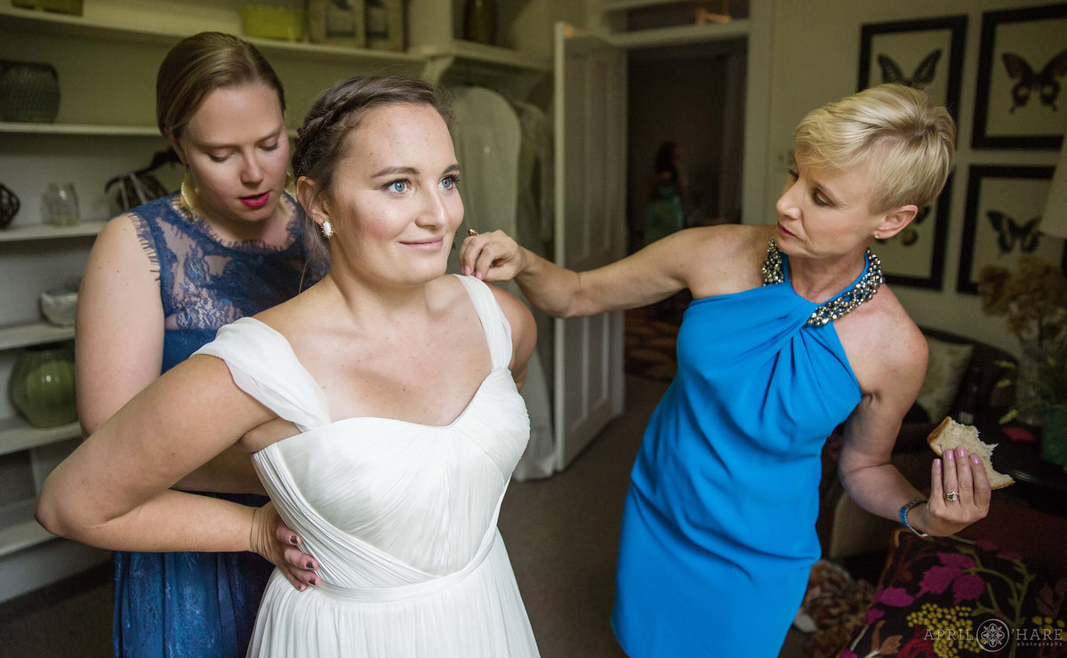 Bride's mom eats a sandwich while helping her daughter get dressed on her wedding day at Chatfield Farms in Colorado