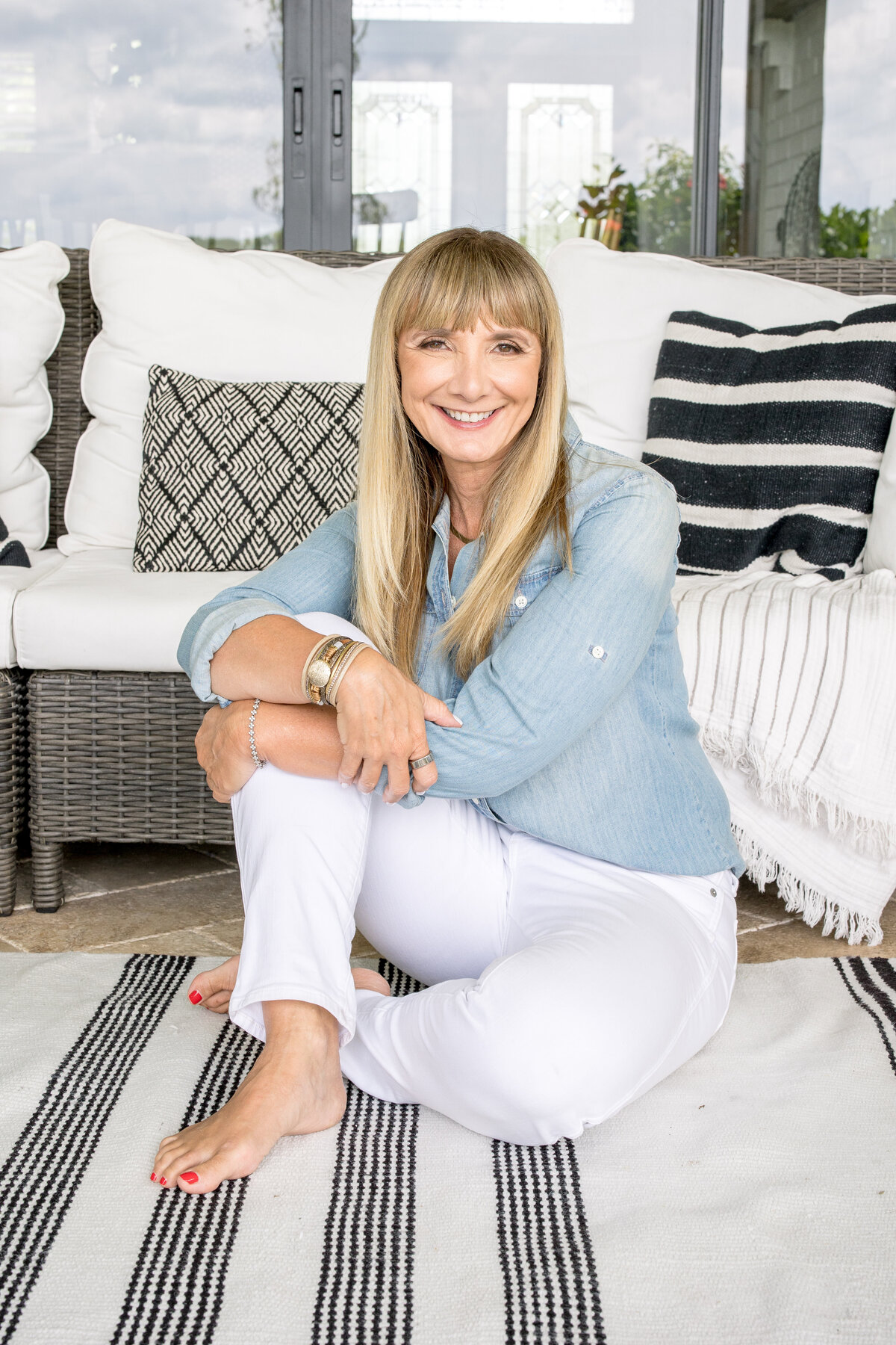 Orlando photographer captures Brand photo shoot in the home of her client as she sits on a black and white rug with her legs crossed as she holds one need to her chest and smiles for her brand photo