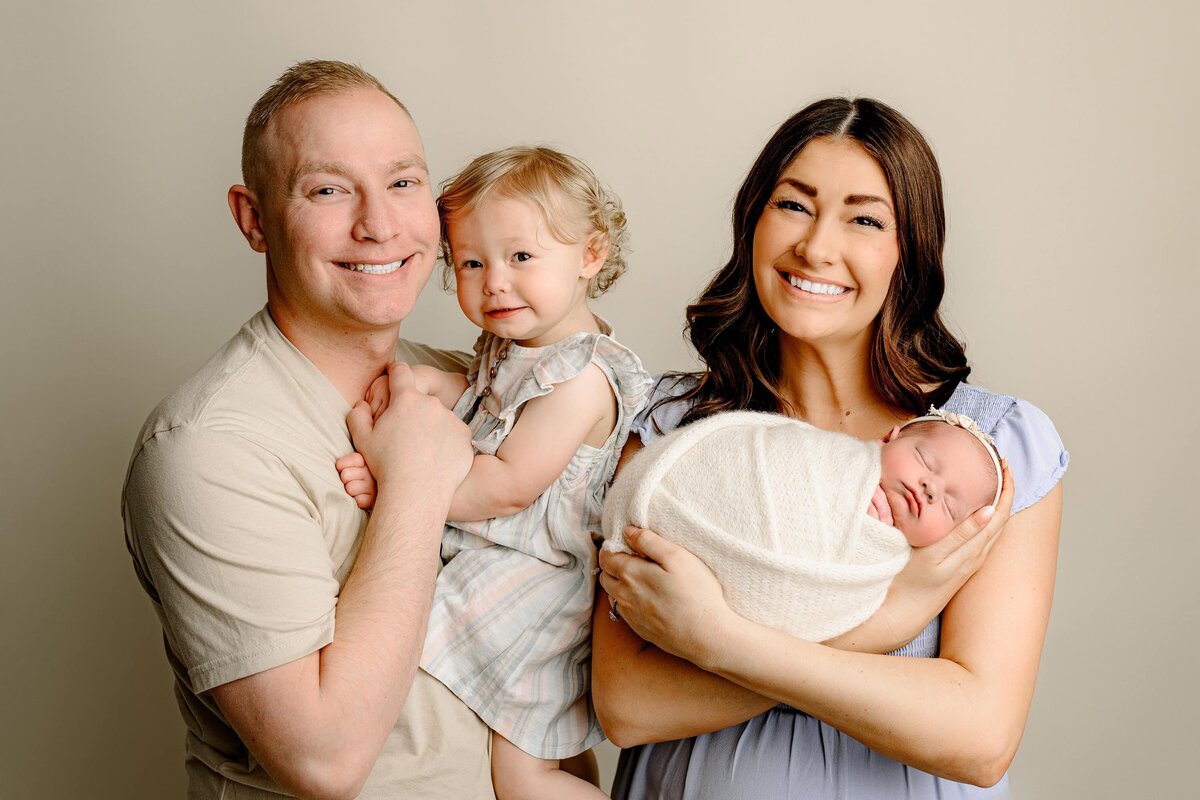 mother and father posed with their 17 moth old daughter and newborn baby in charlotte area studio
