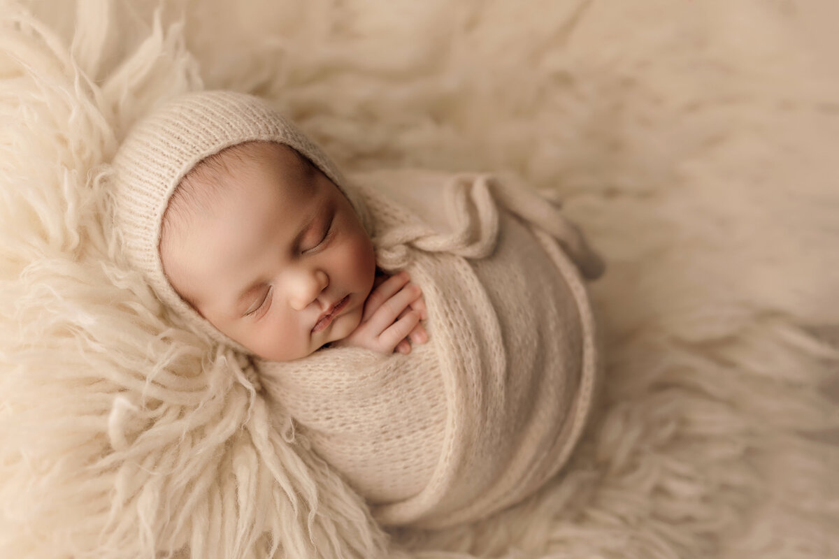 newborn baby boy on cream blanket sleeping