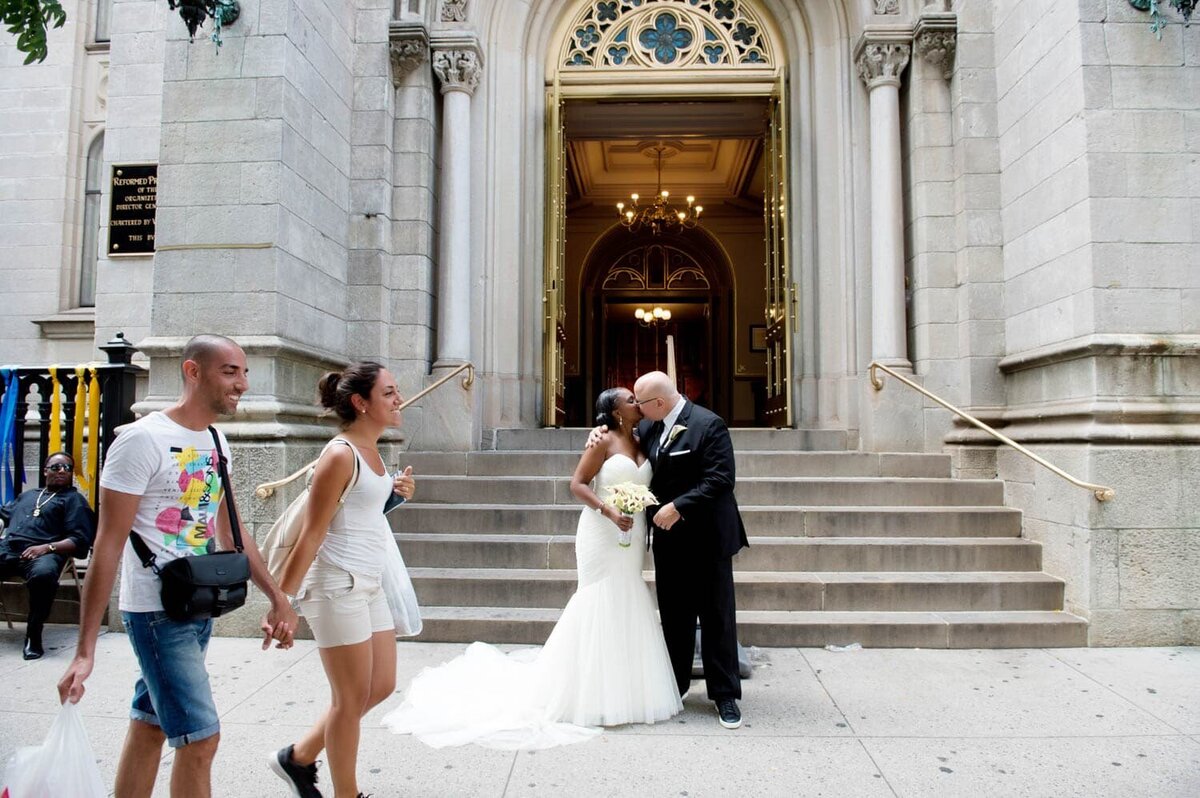 a bride and groom kiss in nyc as passerbys look on and walk past