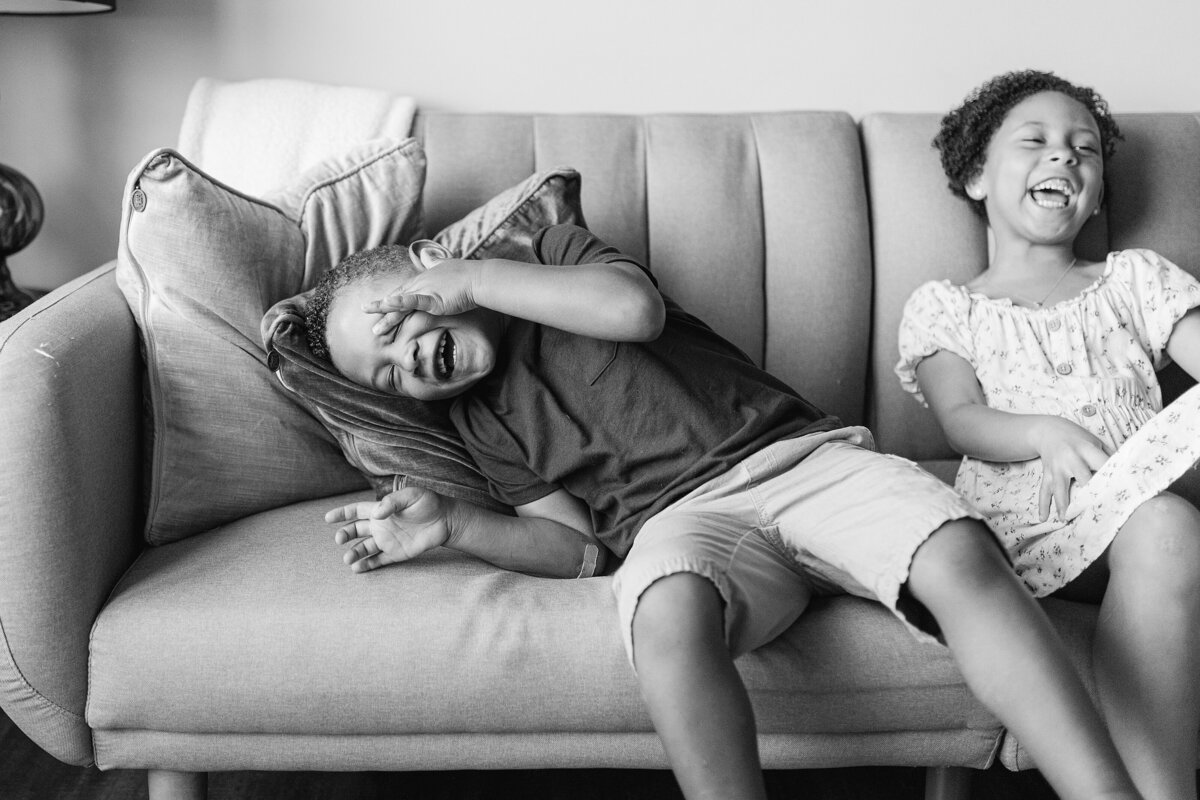 A black and white image of a brother and sister laughing hard on a couch.