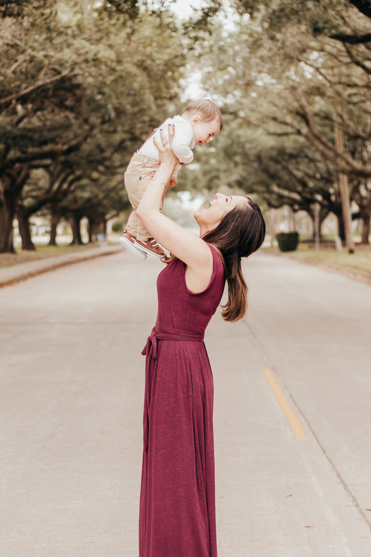 Mother tosses baby in air and giggles with him while standing in the middle of the street in Houston, Texas.