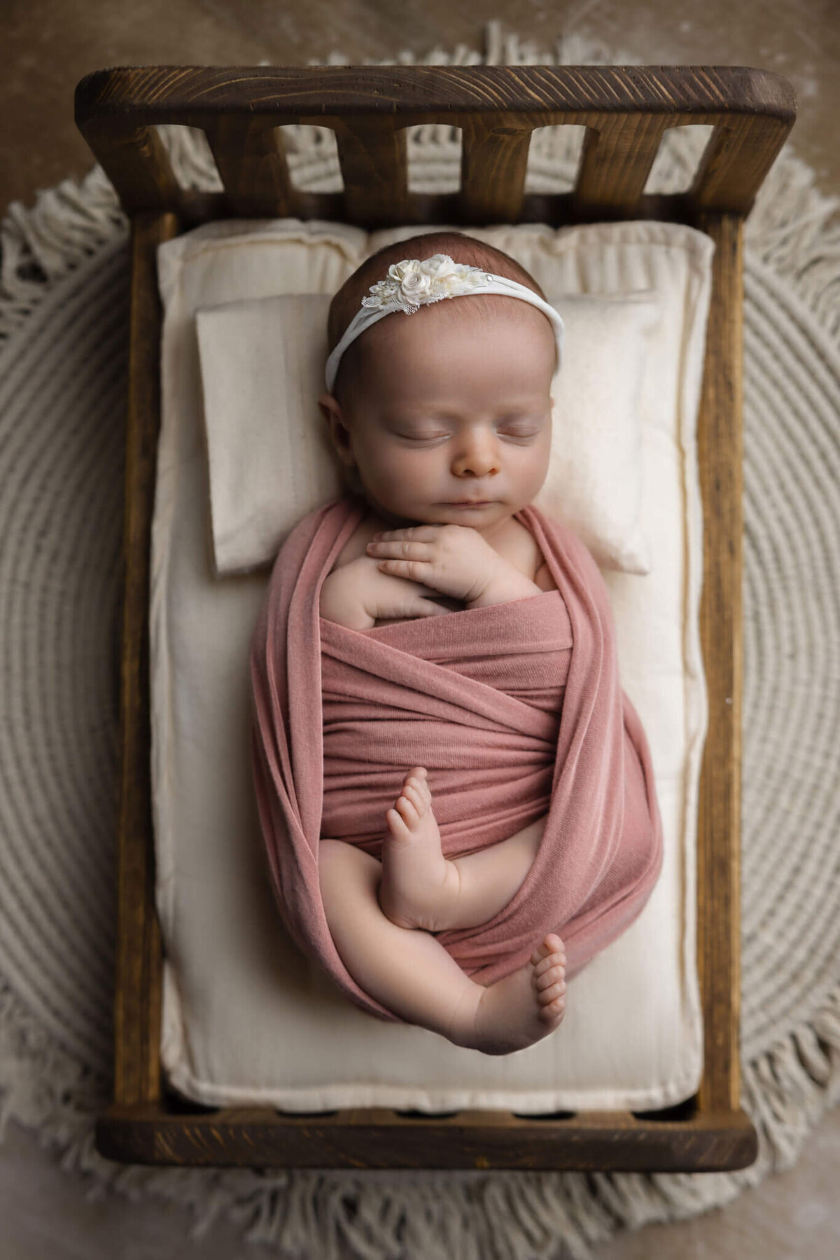 newborn baby wrapped in pink fabric asleep on a tiny wooden bed
