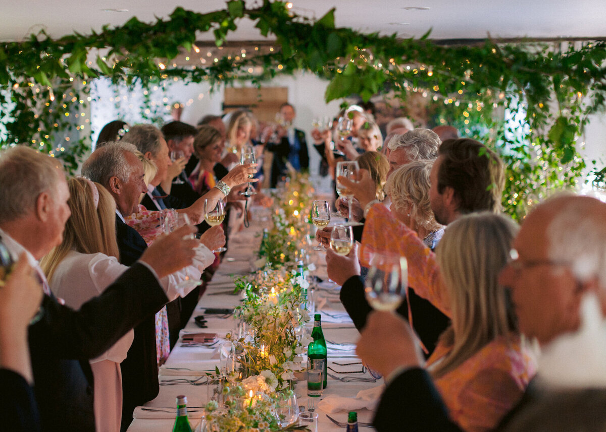 wedding guests standing and rising vine glasses for a toast during wedding speeches at the candle lit barn