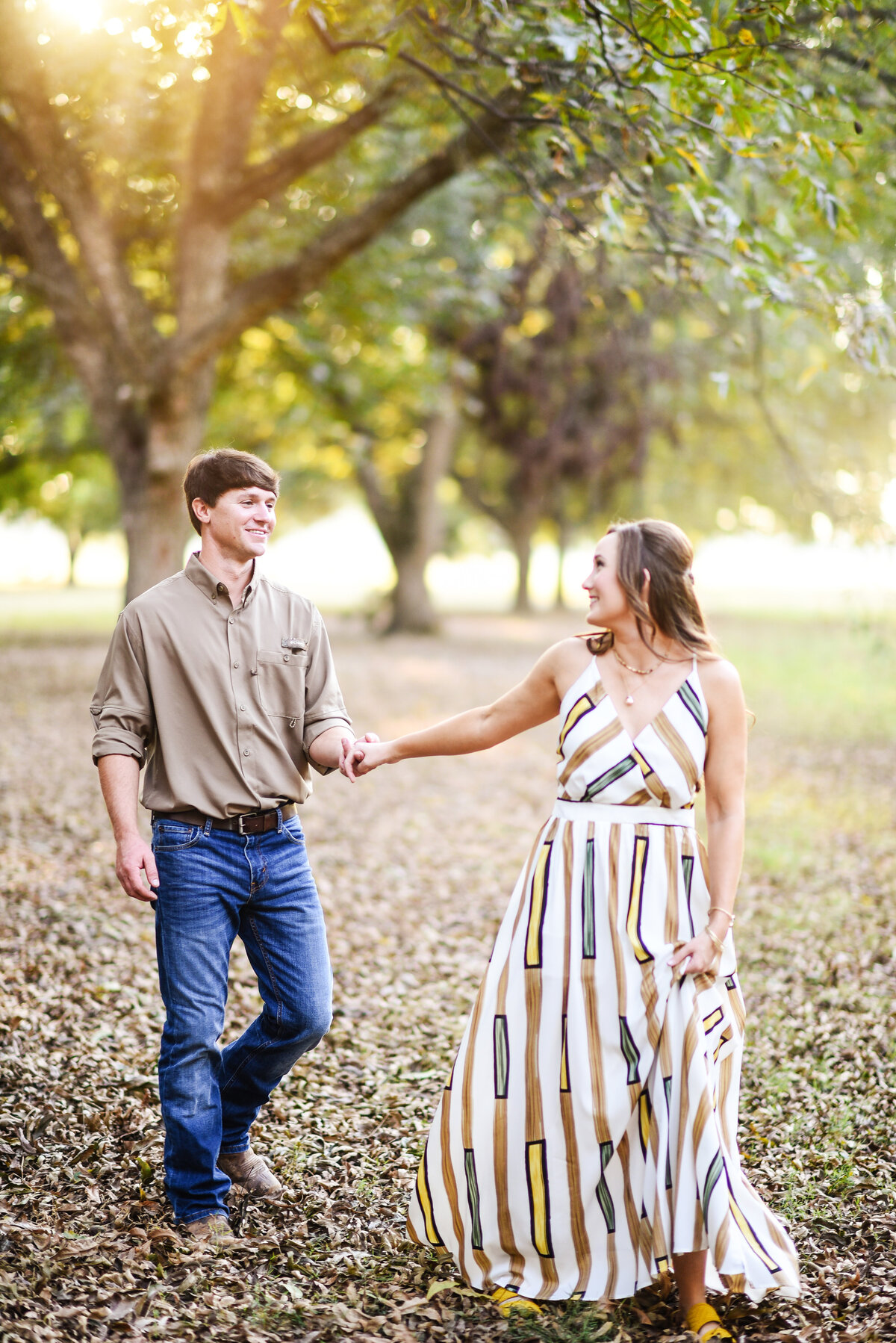 Beautiful Mississippi Engagement Photography: Couple walks hand-in-hand in a sunlit Mississippi delta pecan orchard