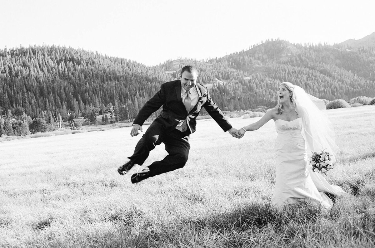 Groom jumping up surprising her bride during portraits in Palisades Tahoe wedding. Black and white film image