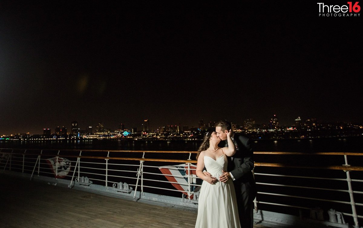 Bride reaches back to kiss her Groom on the Queen Mary at night