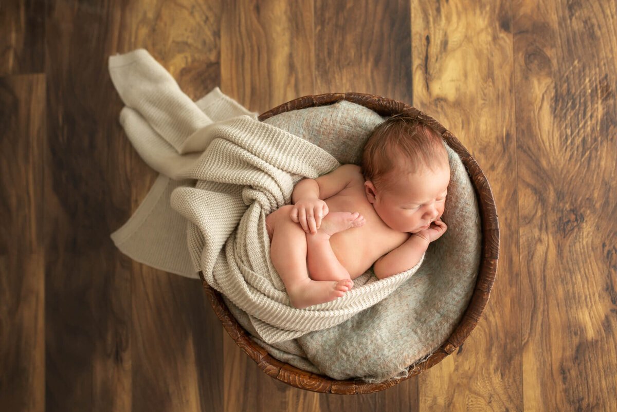 A newborn baby boy  sleeps while wrapped in a blanket and laying in a basket