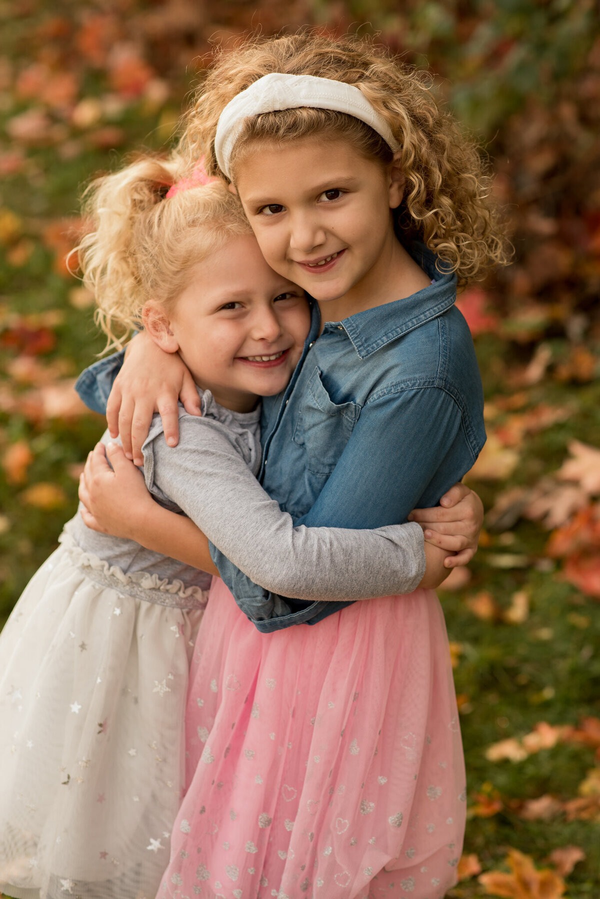Two sisters hugging with fall leaves in background