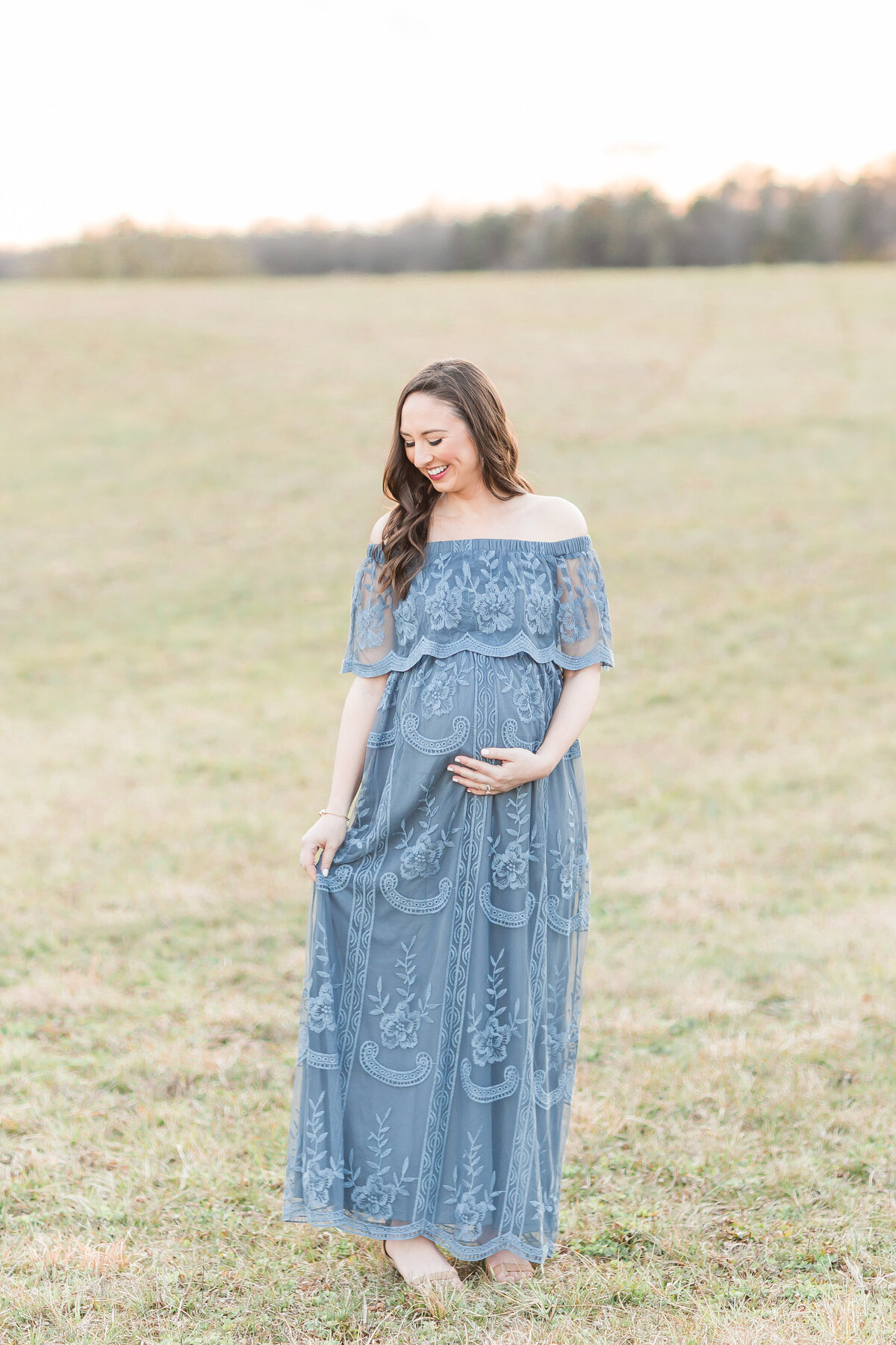 A pregnant mother holding her belly and playing with her dress outdoors by Maternity Photographer DC