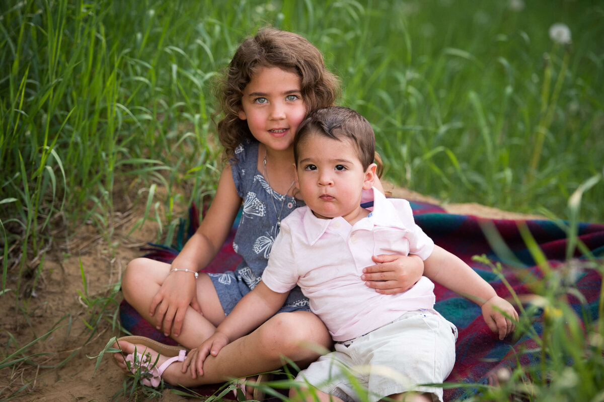 a sister and her toddler brother sitting on a blanket in a grassy field for their family photography session in Ottawa
