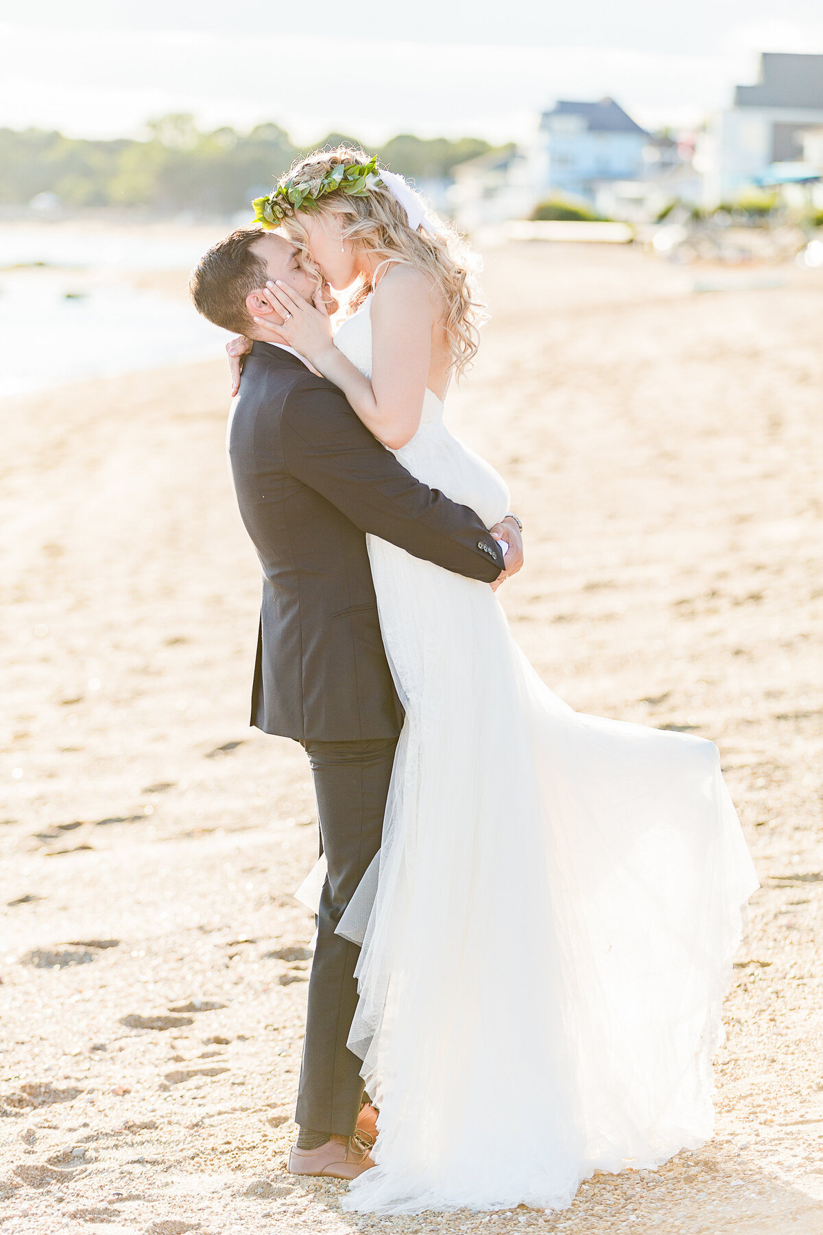 Groom lifts bride on the sandy shores of the Madison Beach Hotel as they share a kiss at golden hour.  Captured by best New England wedding photographer Lia Rose Weddings.