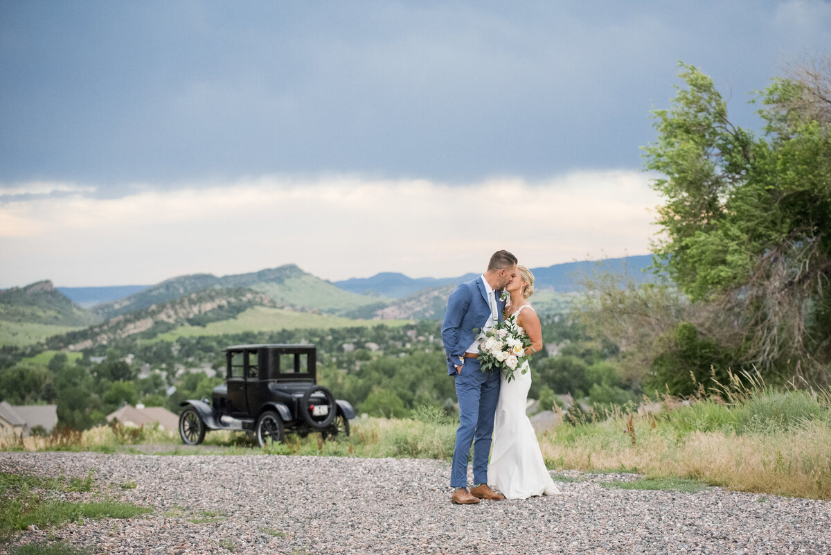 A wide angle shot of the bride and groom sharing a kiss with the vintage stagecoach in the background.