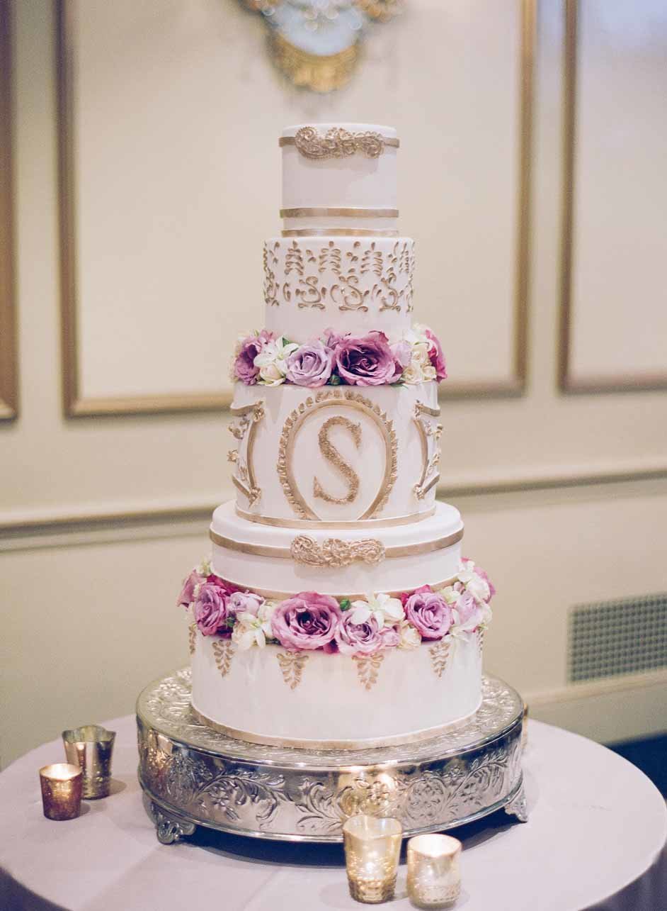 Beautiful white layer wedding cake with gold accents and purple roses.