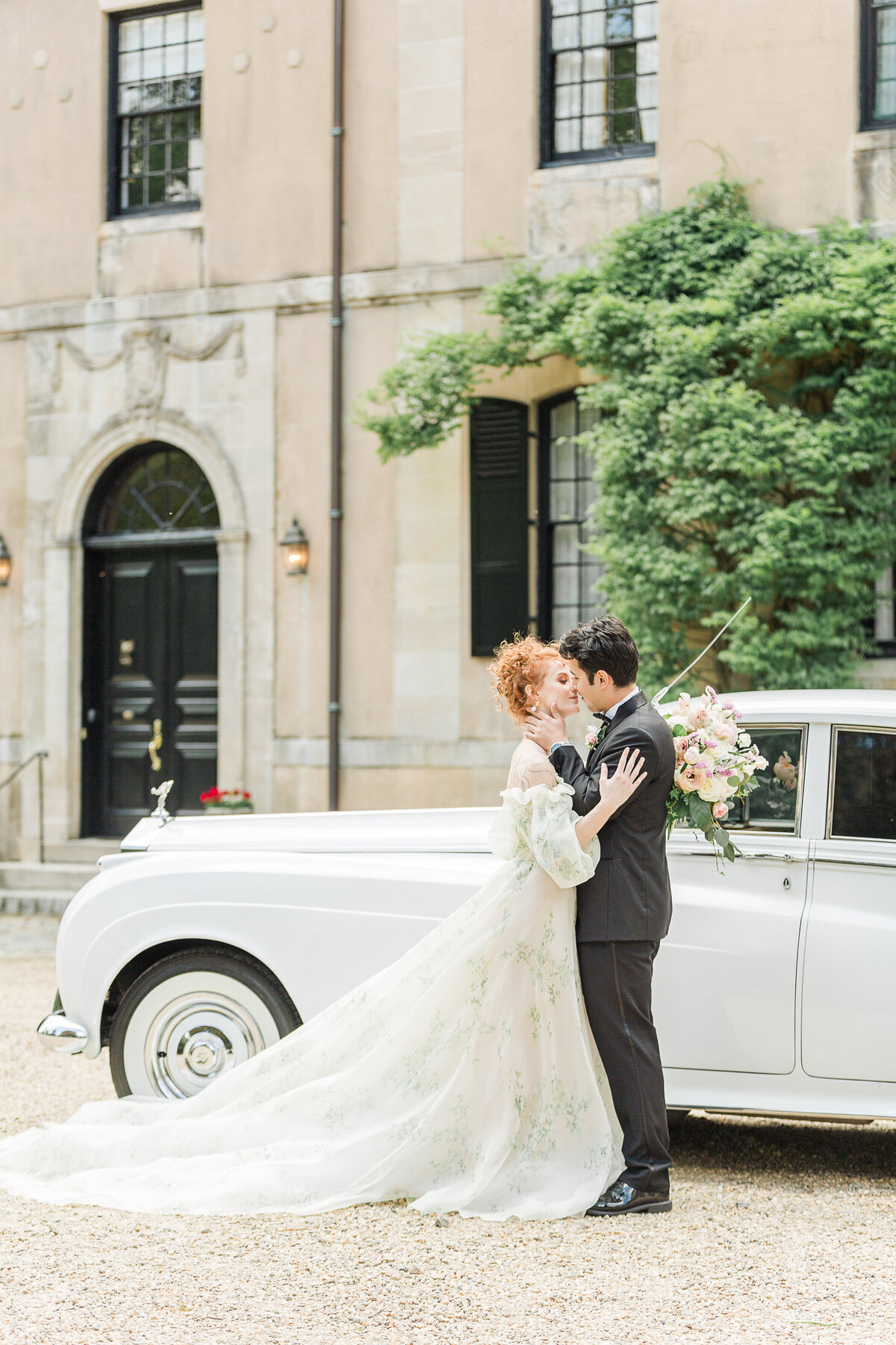 Bride and groom share an intimate kiss at an estate in Boston's North Shore. They are standing in front of a french-inspired mansion and vintage Rolls Royce. Captured by best Massachusetts wedding photographer Lia Rose Weddings