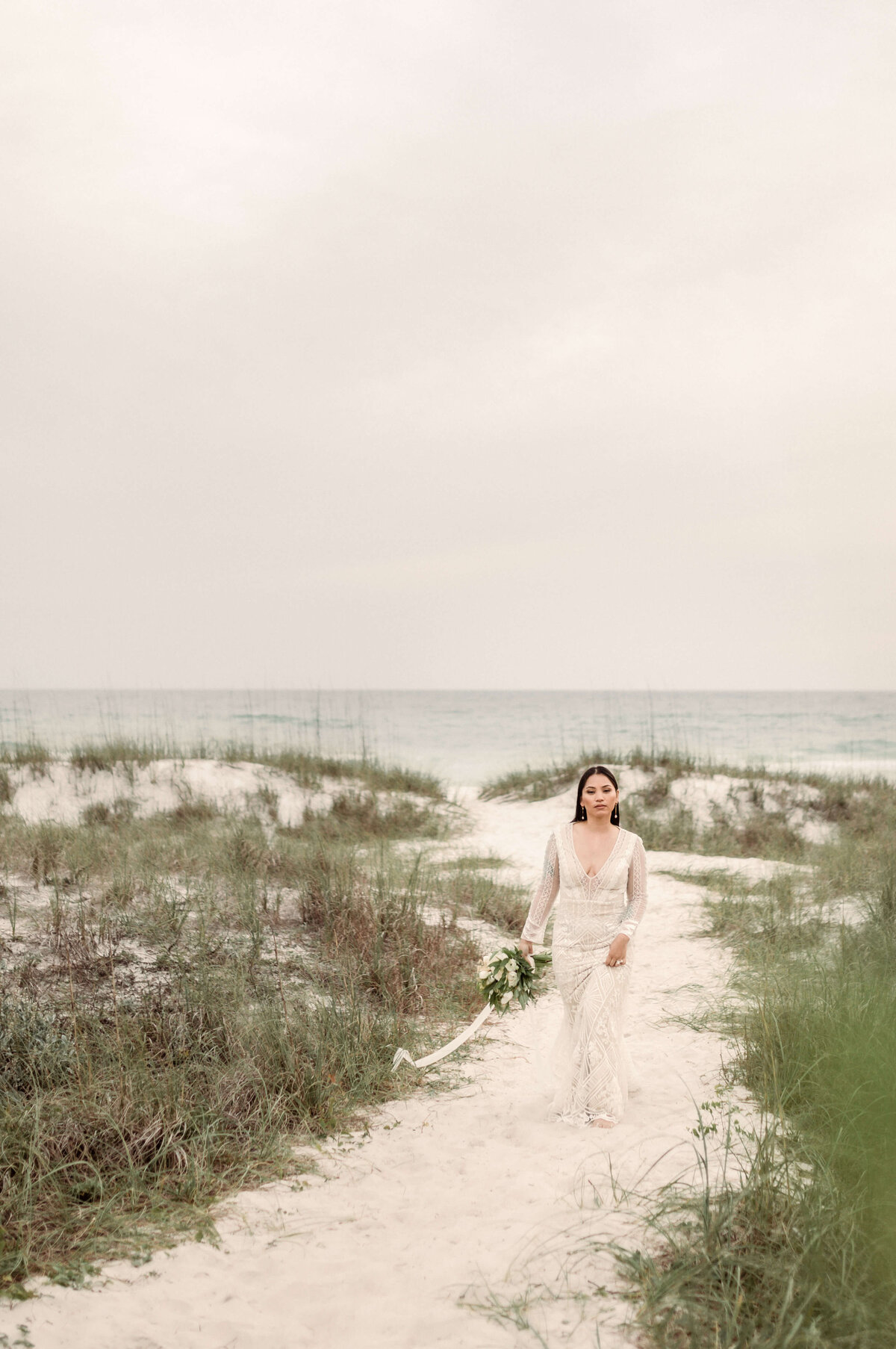 asian bride in bridal dress and veil walks on beach path - taken by panama city fl photographer Brittney Stanley