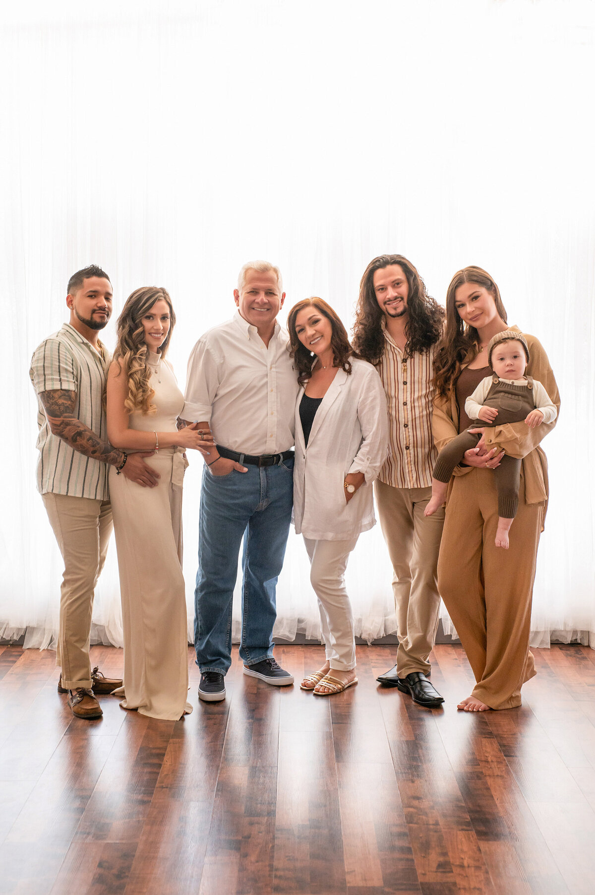 An extended family poses standing in our bright and airy Waukesha photo studio wearing various neutrals.