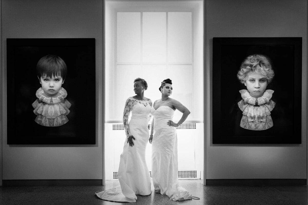 Two brides standing in an art gallery with images on either side of them