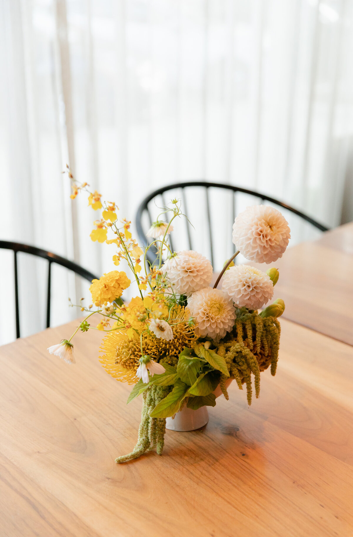 Yellow and pink flowers with greenery form a beautiful bouquet in a vase on top of a wooden table at Chicago wedding.
