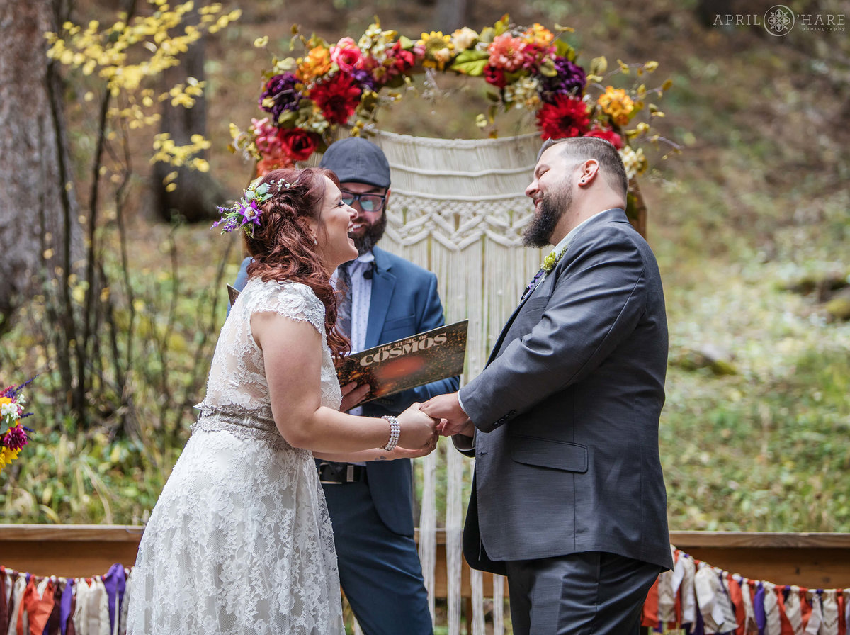 Happy couple laughing in front of their Macrame altar in the forest of Colorado at Beaver Ranch in Conifer