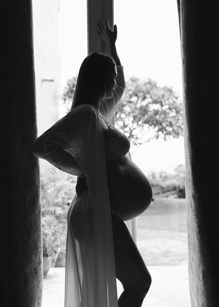 Black and white silhouette of  pregnant mommy standing by the doorway.