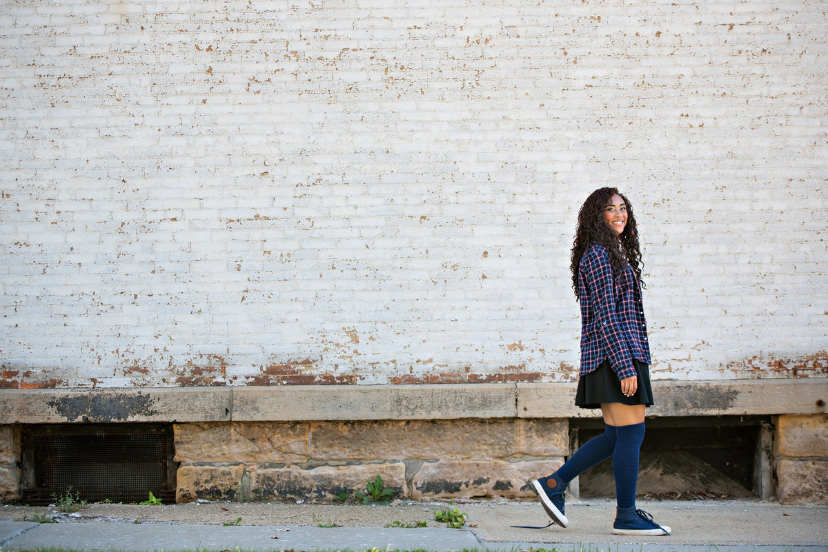 Senior Portrait of a girl walking along a bricked building.