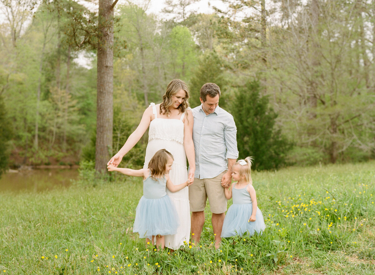 Family plays in a field during their maternity session at Joyner Park in Wake Forest. Photographed by Raleigh Maternity Photographer A.J. Dunlap Photography.